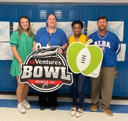 A teacher with her principal and two other people, holding a 68 Ventures Bowl sign