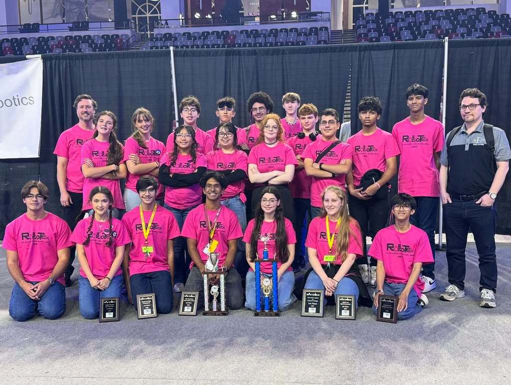 A high school robotics team in pink T-shirts, with trophies and plaques they won
