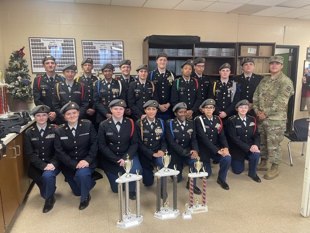 A group of JROTC cadets in uniform, with three trophies