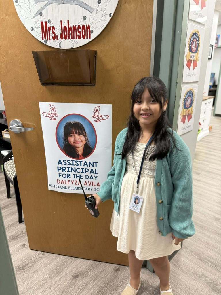 A girl standing in a classroom doorway with a lanyard and a walkie talkie 