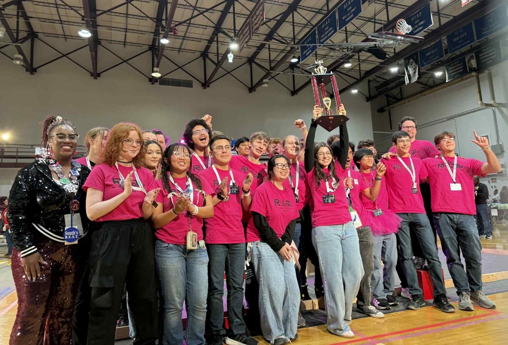 A group of high school students holding up a trophy in a gymnasium