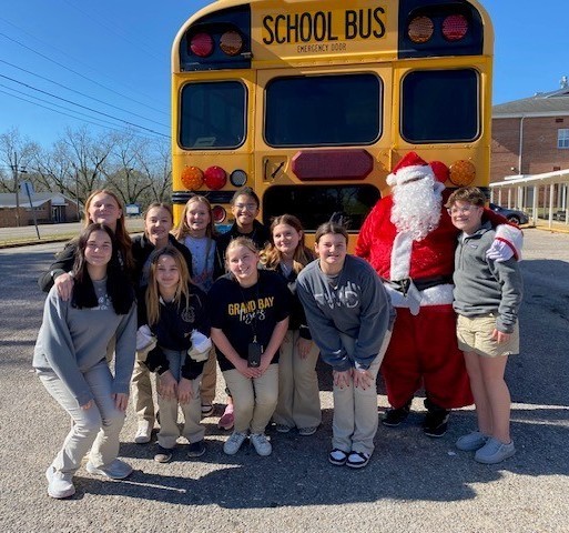 Santa and a group of students standing behind a school bus