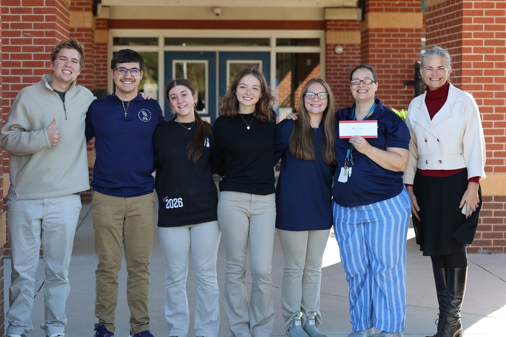 A group of students with two educators, one of whom is holding a check