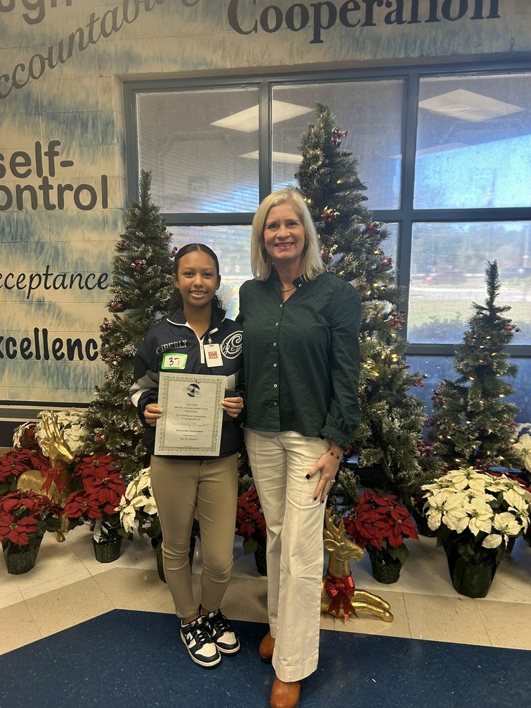 Woman and girl standing in front of a Christmas tree. Girl is holding a certificate and gift card.