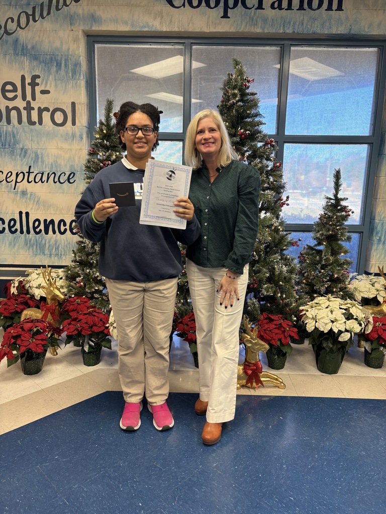 Woman and girl standing in front of a Christmas tree and other decorations. Girl is holding certificate and gift card.