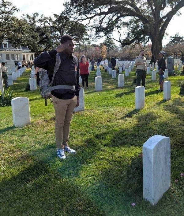 A student standing at attention and saluting at a gravesite