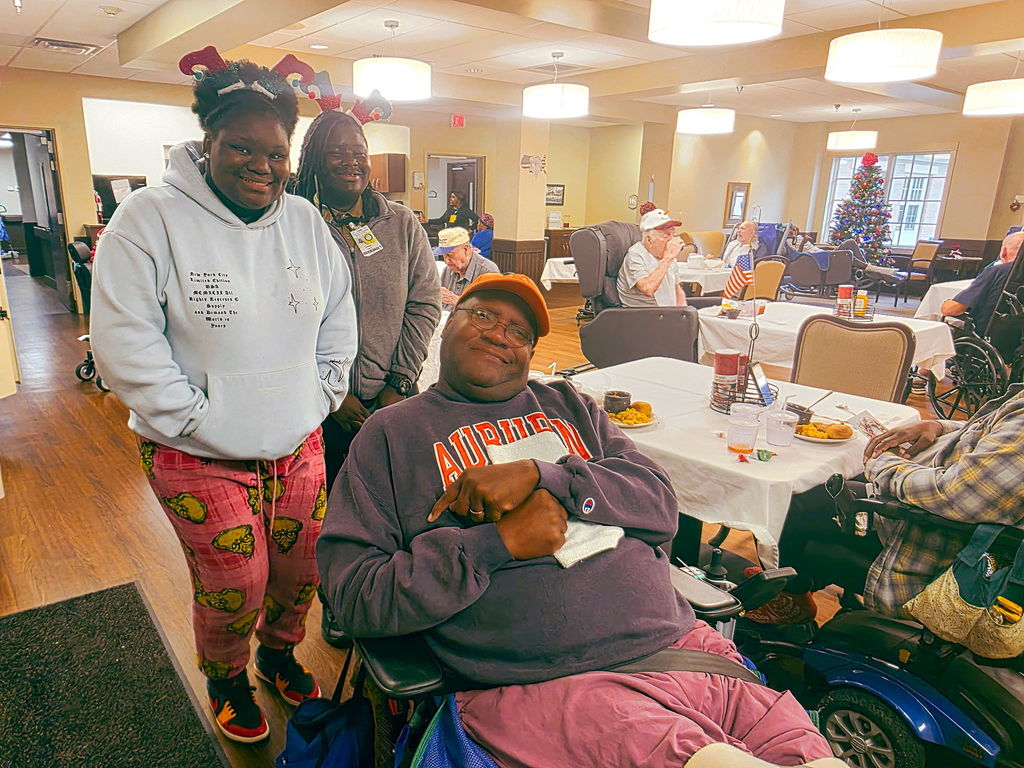 Woman and girl standing with a man that is sitting in a wheelchair