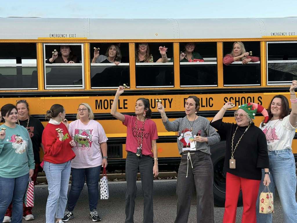 Teachers standing outside a school bus and others looking out the windows, ringing bells