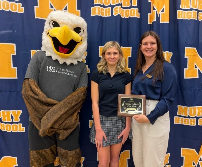 A high school girl and her coach stands with the U.S. Sports University's eagle mascot