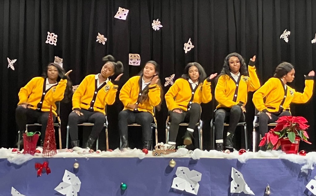 A row of high school girls in yellow cardigans acting out a dance move