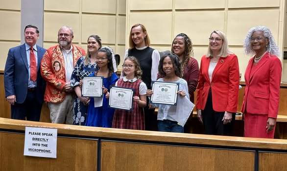 Three students holding certificates, standing with a group of adults