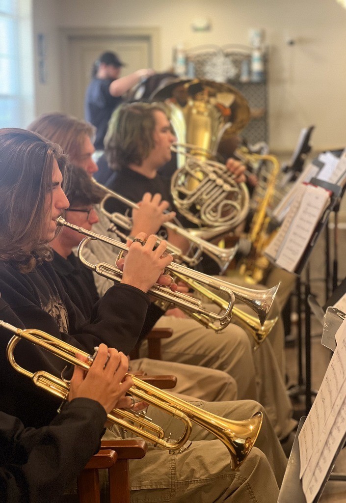 A row of high school students playing trumpets and one playing a French horn
