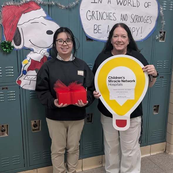 A student holds a gift, while a teacher holds a sign for the Children's Miracle Network