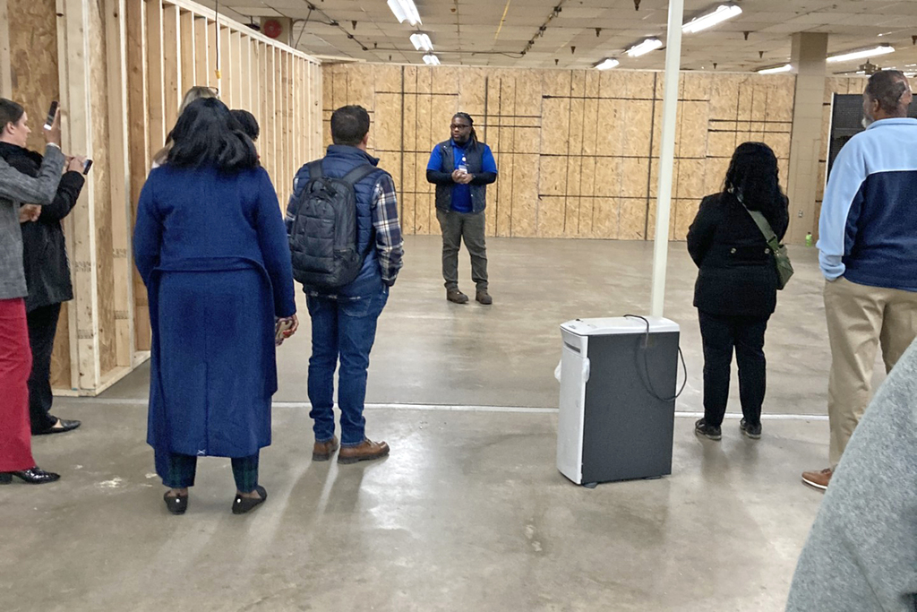 A man stands in a carpentry workshop, talking with a group of people
