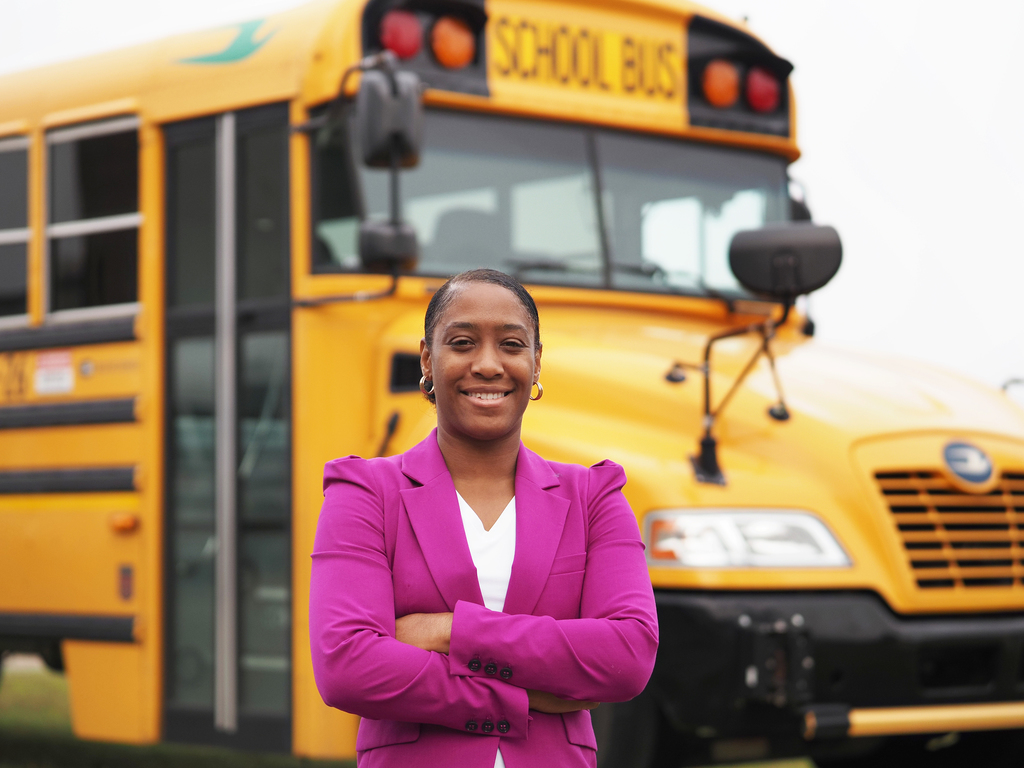 A woman standing with her arms crossed in front of a school bus