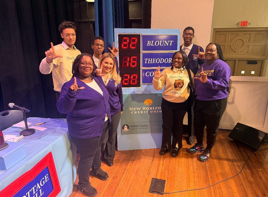 A group of smiling students standing in front of a scoreboard