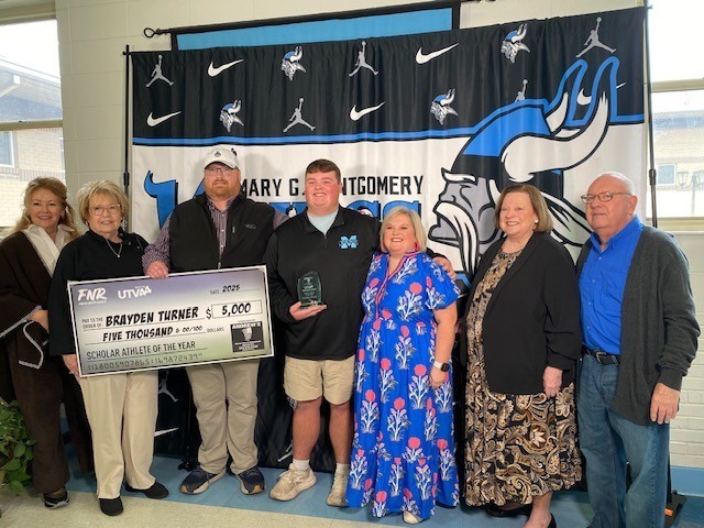 A high school boy holding an award, surrounded by his parents and grandparents, with a large check for $5,000