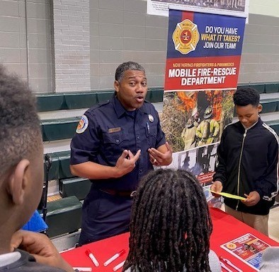 A fireman in uniform speaks to a group of students