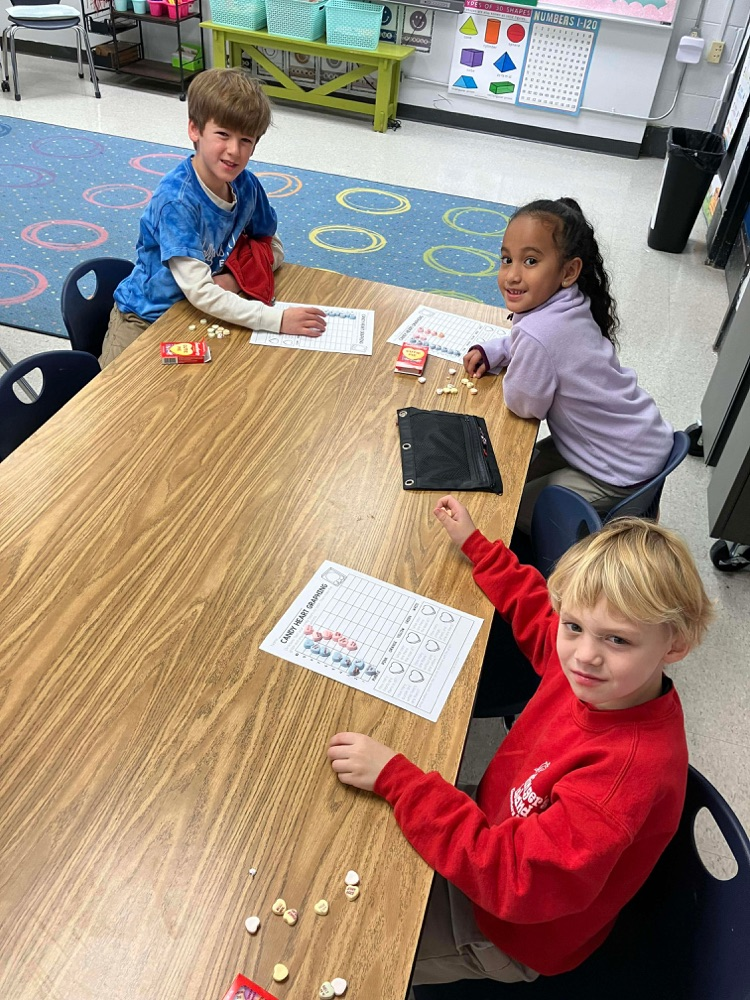 3 students at a tables using candy hearts to create a graph