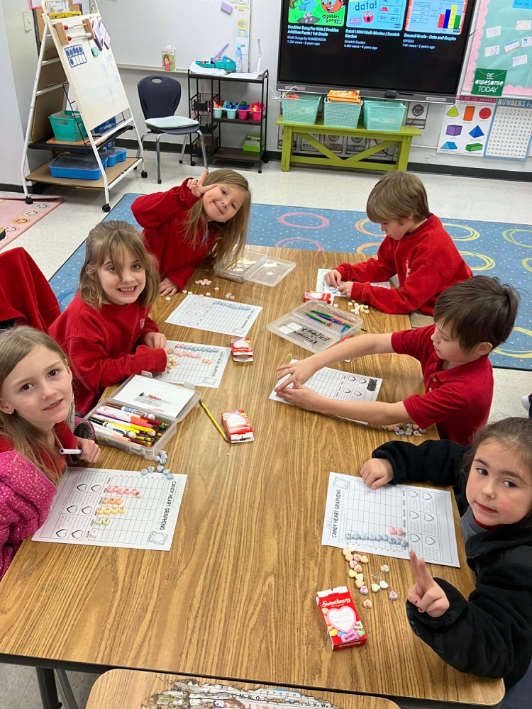 group of students at a table using candy hearts to create a graph