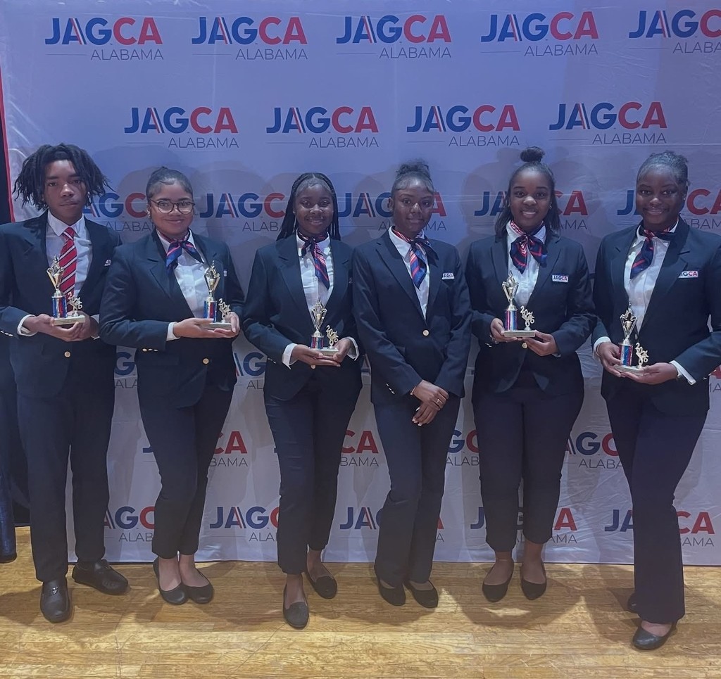 Six students wearing blazers, five of whom are holding trophies