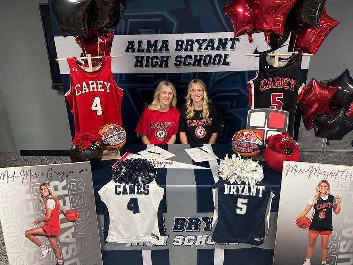 Two high school girls sitting behind a table with basketballs and basketball jerseyes