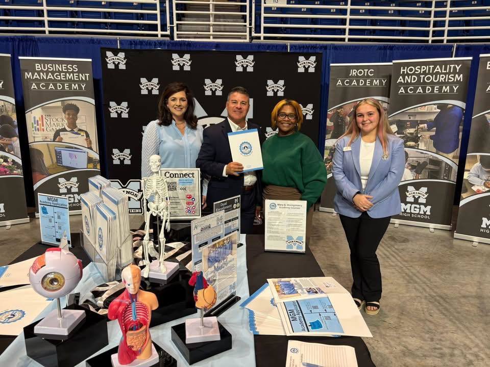 Three teachers and a student standing in front of banners at the signature academy showcase.