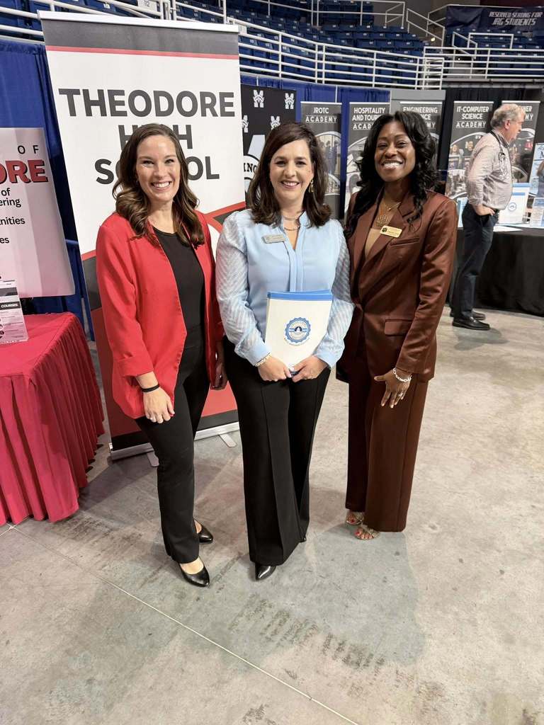 Three teachers standing in front of banners about signature academies offered in Mobile County Public Schools. 