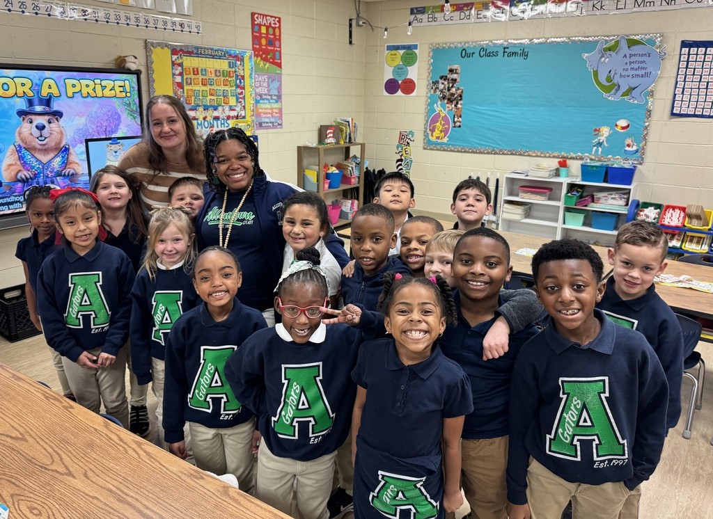 A teacher and a high school student in a classroom with a bunch of elementary students in shirts with a big "A" on them