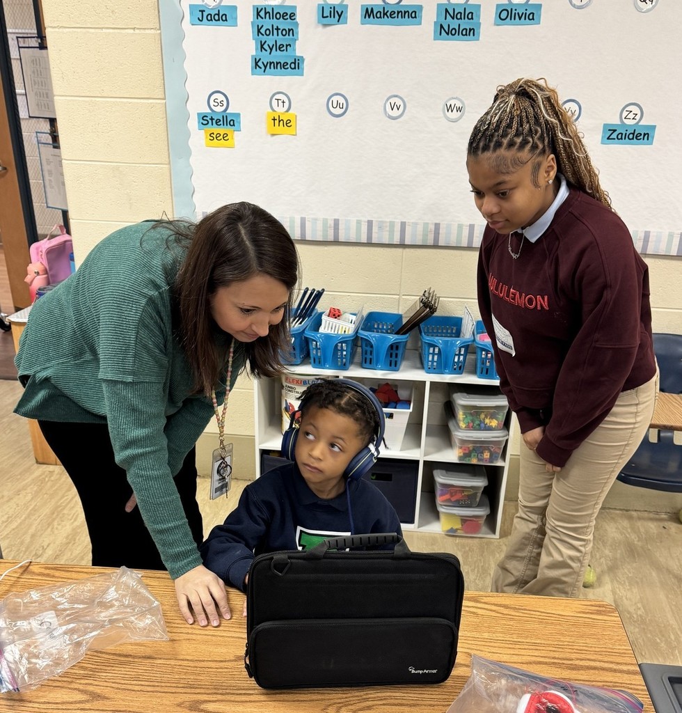A teacher and a high school student help an elementary student with his laptop