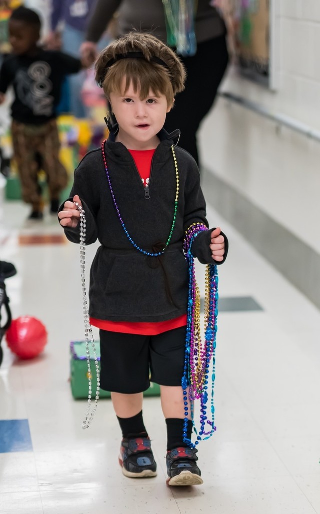 A boy carrying Mardi Gras beads in a hallway