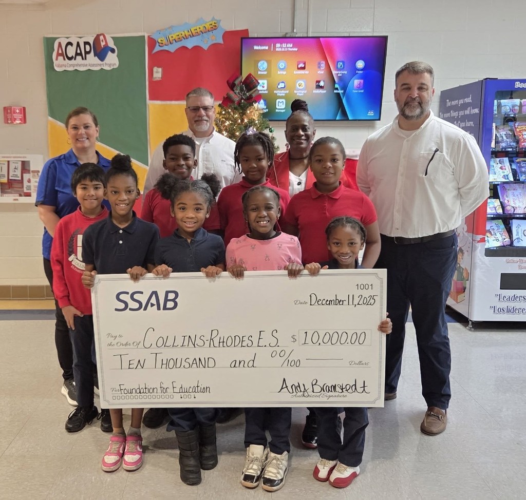 A group of students and a few adults, with an oversized check for $10,000 made out to Collins-Rhodes Elementary