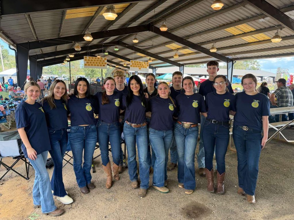 A group of students in jeans and blue T-shirts, standing in a barn