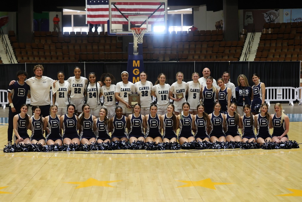 A basketball team and cheerleaders pose for a group photo on a basketball court