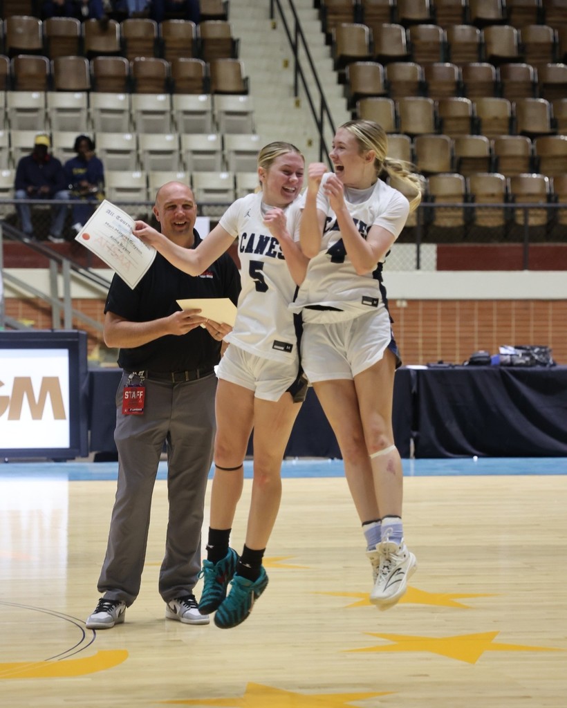 Two high school basketball players celebrate while a smiling man looks on