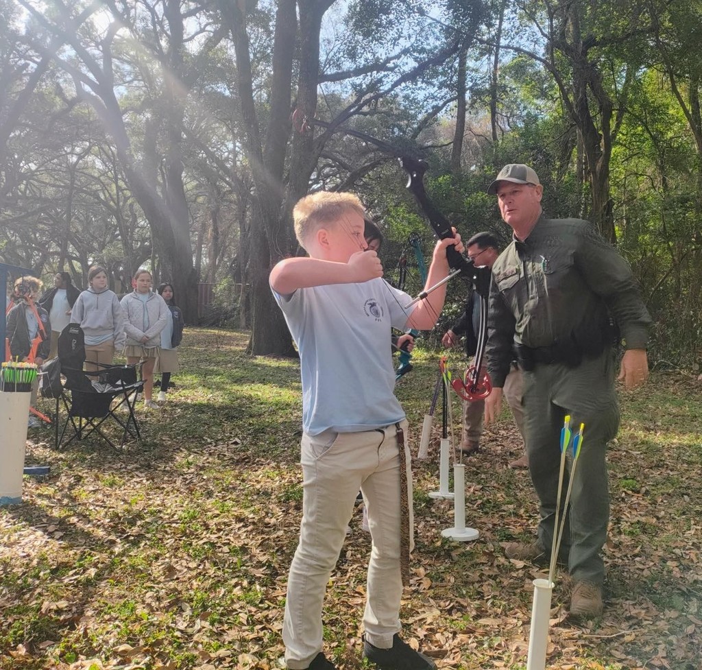 A man watches a boy with a bow and arrow
