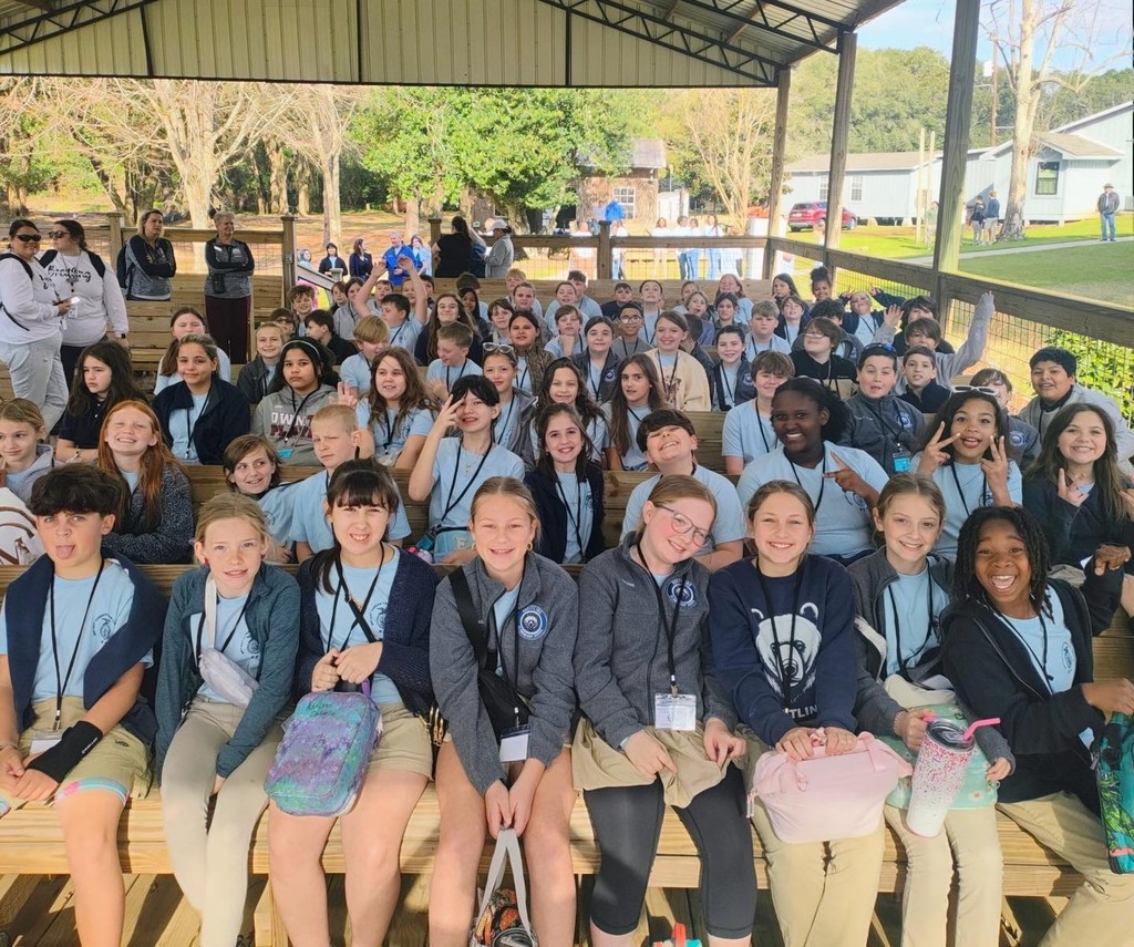 A large group of elementary students seated on benches on a covered patio