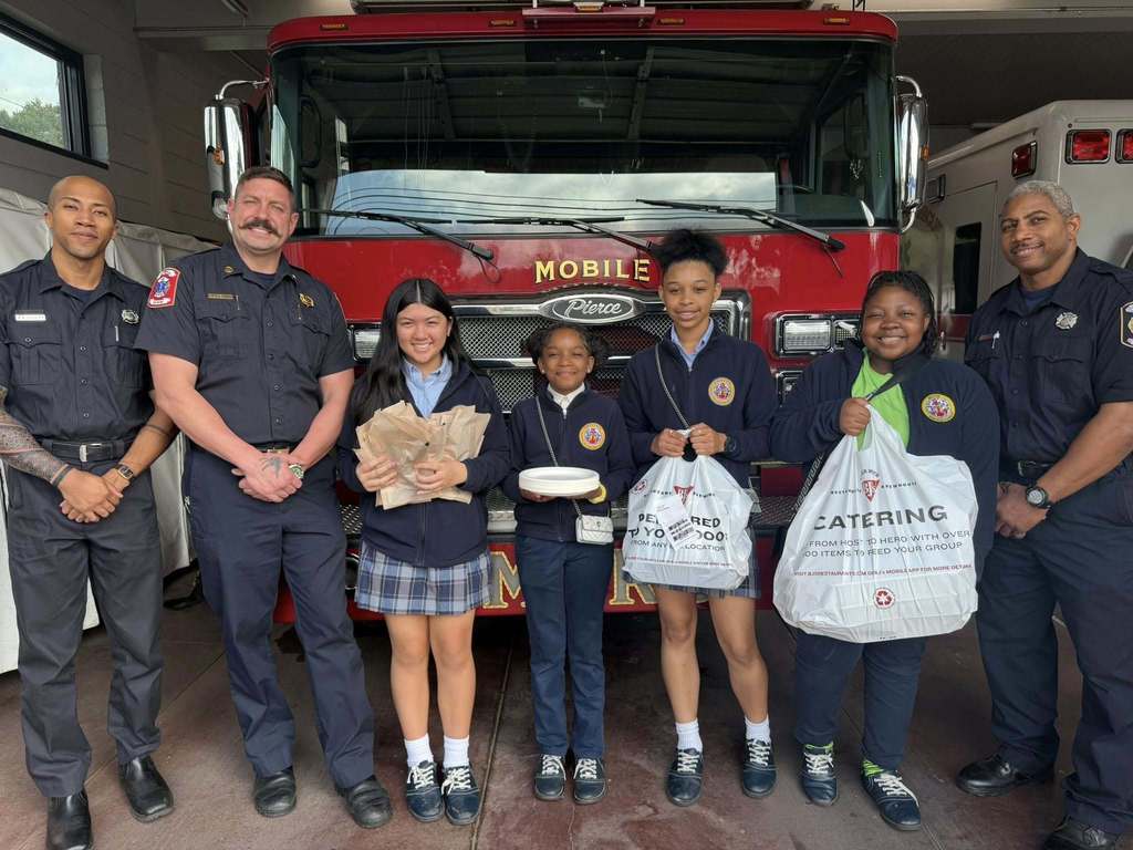 Four students holding bags of food, standing with three firefighters in front of a fire truck
