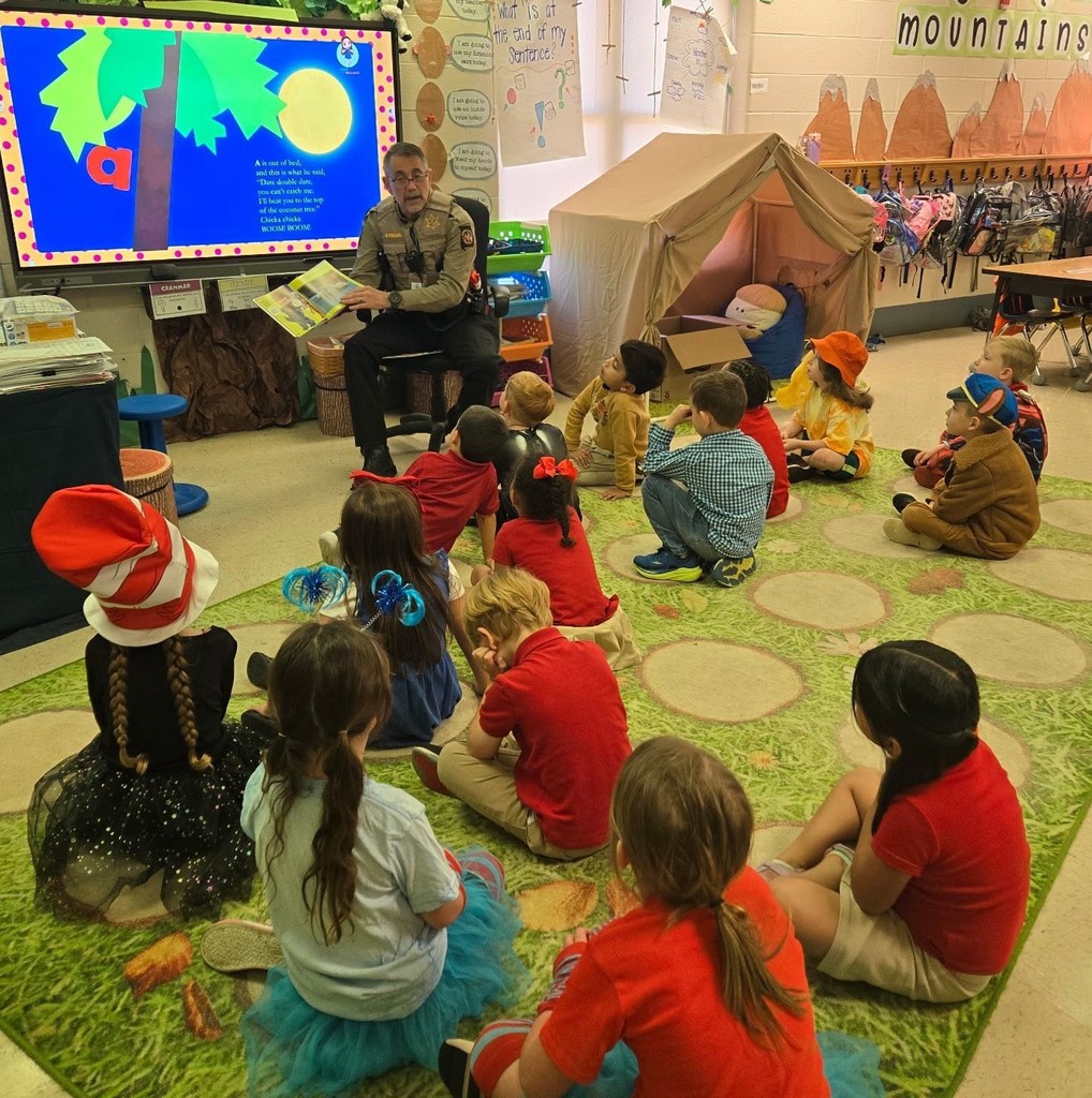 A man in a sheriff's office uniform reads to a classroom full of children