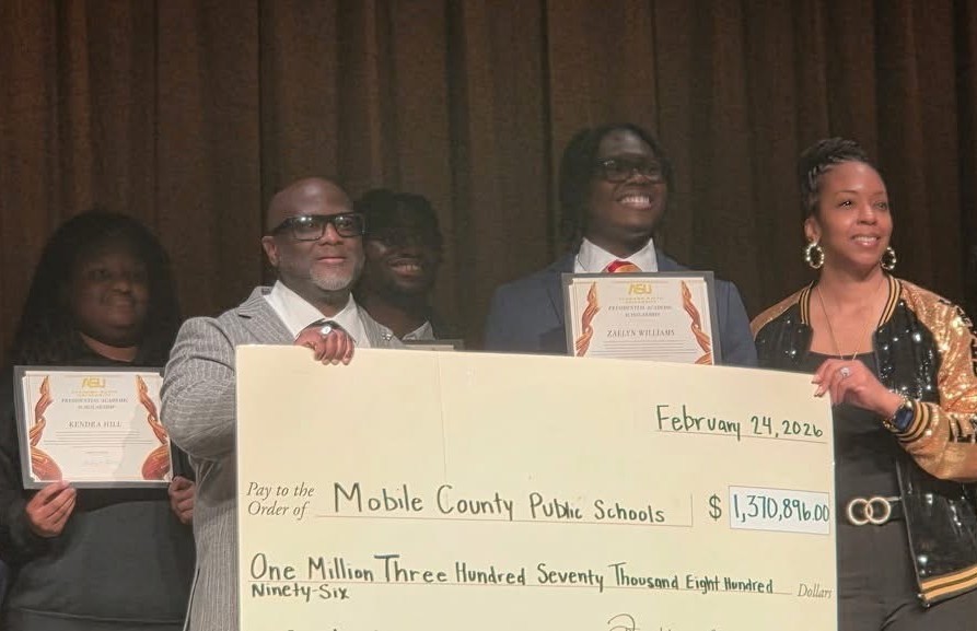 Two adults holding an oversized check while students behind them hold certificates