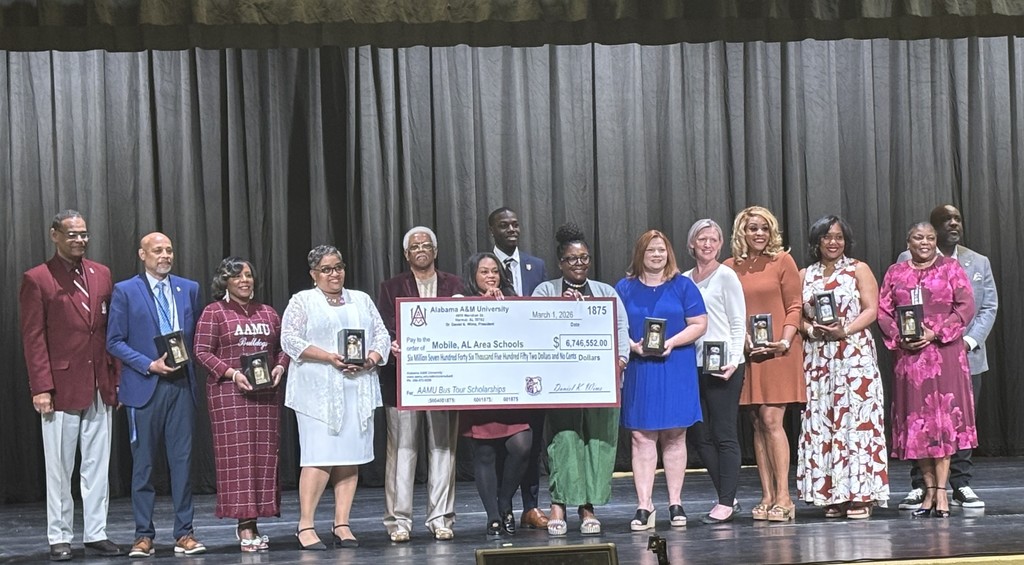 A group of adults standing on a stage with an oversized check bearing the logo of Alabama A&M University
