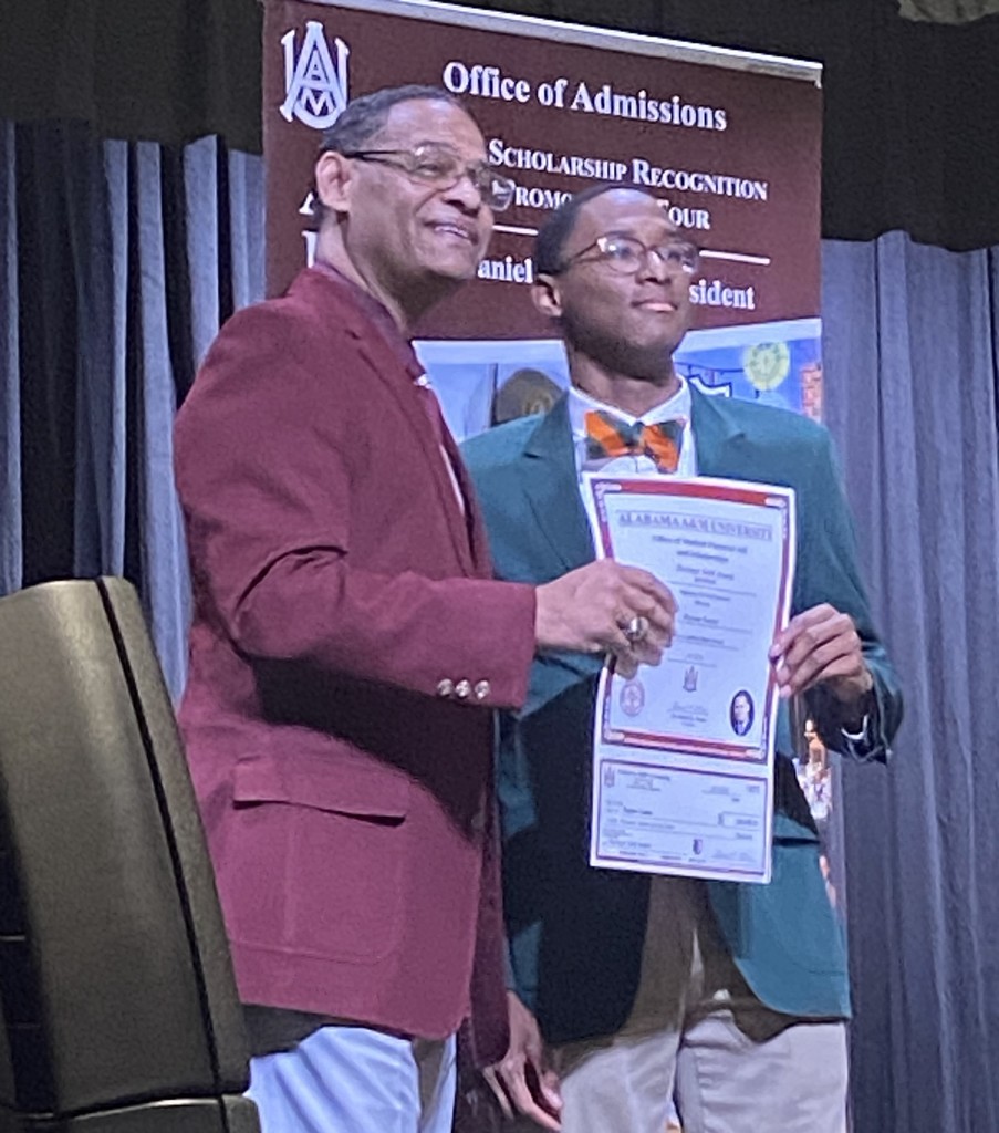 A man in a maroon blazer stands with a LeFlore student, holding a certificate