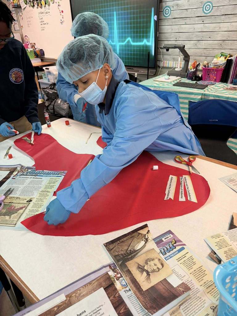 A student in hospital scrubs working with information cut out from newspapers and other publications