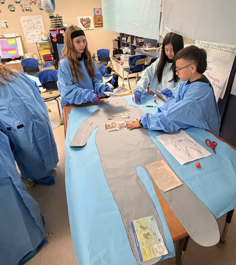 Three students in hospital scrubs placing pieces of paper on a cutout of a person