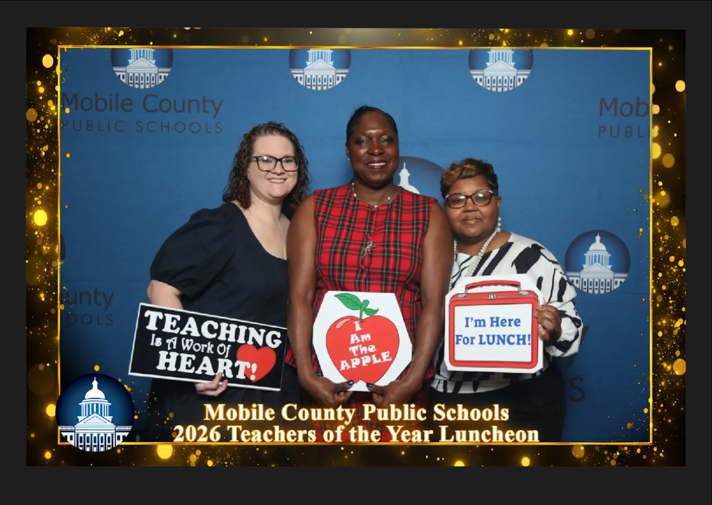 Three educators pose together in front of a “Mobile County Public Schools 2026 Teachers of the Year Luncheon” backdrop, each holding a celebratory sign, including messages such as “Teaching is a Work of Heart,” “I Am the Apple,” and “I’m Here for Lunch.”