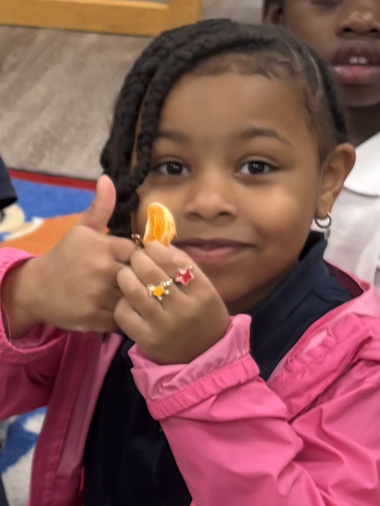A girl holding a piece of orange and giving a thumbs up