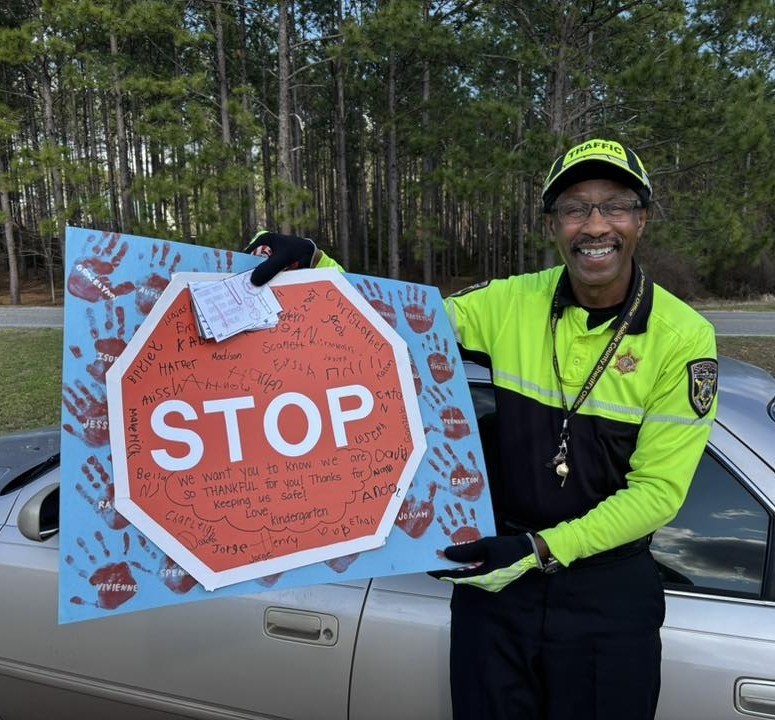 A school crossing guard holds a hand-drawn sign with a stop sign on it
