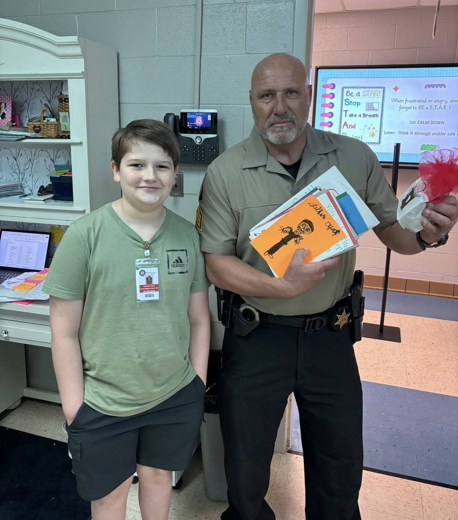 A Wilmer Elementary student stands with a sheriff's deputy, who is holding a handful of handmade cards
