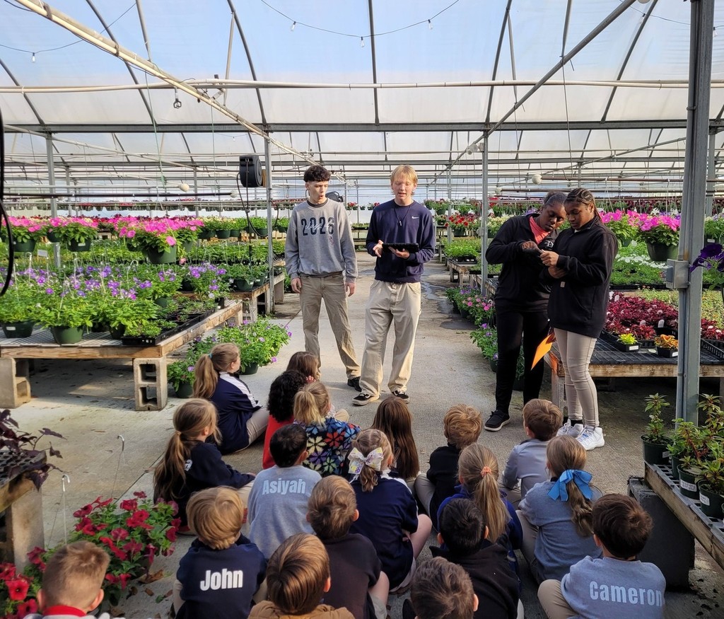 High school students talk with first-graders in a greenhouse