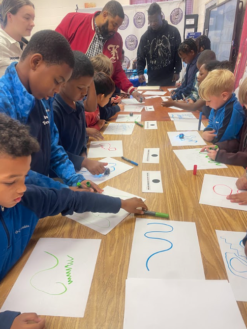 multiple Students looking at drawings on a piece of paper. The drawings depict a path of which the students created for their robot to follow 